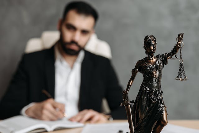 a%20statue%20of%20lady%20justice%20with%20a%20lawyer%20in%20the%20background a%20statue%20of%20lady%20justice%20with%20a%20lawyer%20in%20the%20background